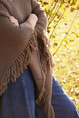 Poncho tejido en lana merino color crudo, con cuello alto y etiqueta de cuero con logo en la espalda.