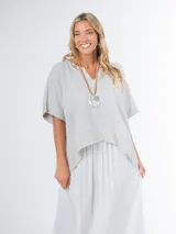 Blusa tipo poncho confeccionada en lino italiano, color gris claro, con escote en V y calce amplio.