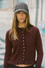 Cárdigan gris jaspeado de punto con cuello redondo y manga larga. Presenta volantes en el borde de los botones, en el bajo y en los puños.