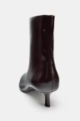 Botín color bordó con efecto acharolado, caña baja, tacón kitten de 4 cm y punta fina. Cierre mediante cremallera lateral.