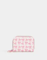 Billetera pequeña de cuerina color blanco con estampado de lazos rosas y corazones. Tiene cierre circundante y tirador de goma.