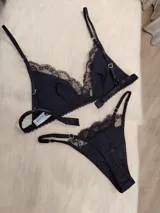 Conjunto de lencería negro, compuesto por un corpiño triangular de algodón con detalles de encaje y una tanga de algodón con detalles de encaje.