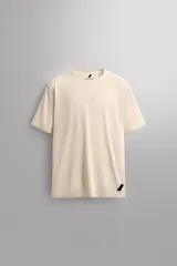 Camiseta deportiva color beige confeccionada en tejido técnico ligero y elástico con estructura perforada. Tiene cuello redondo, manga corta, bajo asimétrico con aberturas laterales y logo estampado.