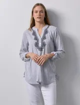 Blusa de gasa bambula a rayas verticales celestes y blancas, con cuello a la base, escote en V con botones y bordado floral negro. Mangas largas regulables con presilla y botón.