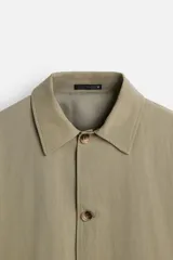 Gabardina color beige de corte amplio, con cuello solapa, manga larga, bolsillos laterales con solapa y cierre frontal con botones.