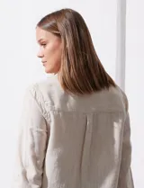 Camisa color beige de lino, marca Dash. Tiene cuello con solapa, abertura central con botones, bolsillo aplicado en el pecho y mangas largas regulables con presilla y botón.