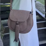 Bandolera marrón con solapa curva y cierre magnético. Presenta costuras decorativas en la solapa, bolsillo tipo guantera frontal y tassel decorativo. Incluye correa larga regulable y bolsillos internos.
