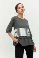 Remera gris con mangas 3/4, corte recto y detalle de volados en el ruedo. Presenta una franja horizontal con estampado de rayas verticales blancas y negras.