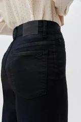 Pantalón de jean negro de tiro alto y pierna palazzo, confeccionado en denim con elastano y coating negro con apariencia similar al cuero.