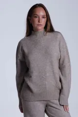 Sweater color beige de tejido de punto con cuello alto y mangas largas. Presenta detalles de ochos en diagonal en los laterales.