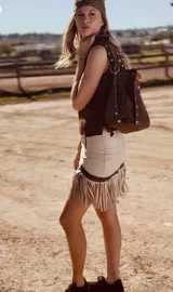 Bolso tipo bucket de cuero color marrón con tachas plateadas. Tiene correa larga regulable para usar al hombro y cierre con cordón ajustable.