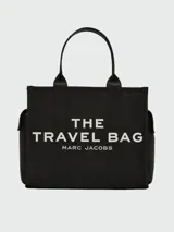 Bolso tote de lona color negro, con asas de mano y correa de hombro. Estampado frontal con el texto "THE TRAVEL BAG MARC JACOBS" en color blanco.