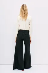 Pantalón de jean negro de corte oxford, tiro medio, con cintura y cadera ajustadas, y piernas anchas con recortes laterales.