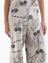 Pantalón de punto de tiro alto, pierna ancha y cintura elastizada. Presenta un estampado integral en tonos grises y negros sobre fondo beige claro, con motivos de cerezas, figuras estilizadas y cadenas.