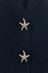 Chaqueta azul marino de punto con escote pico y manga corta. Cierre frontal con tres botones dorados en forma de estrella.