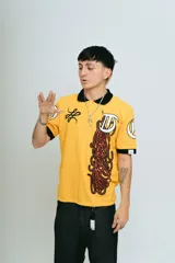 Chomba amarilla de piqué con cuello y puños negros, corte regular, bordado y aplique premium.