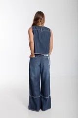 Blusa sin mangas de denim oscuro, con cuello redondo y costuras contrastantes en color marrón claro. Presenta un pequeño parche rectangular multicolor en la parte inferior frontal. El ruedo es deshilachado.