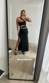 Vestido largo negro con abertura lateral, top asimétrico con un solo tirante y abertura en la cintura con hebilla dorada.