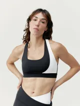 Top deportivo bicolor negro y blanco con asimetría, sujeción media-alta y tirantes cruzados. Confeccionado en tejido Shape_Tech con interior de mesh y copas extraíbles.