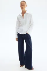 Camisa entallada blanca de manga larga con cuello clásico, tapeta de botones parcialmente abierta y pinzas delanteras y traseras para estilizar la figura.