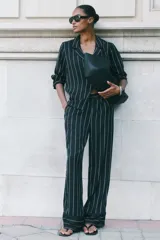 Pantalón holgado negro con finas rayas verticales blancas, tiro alto, cintura elástica, bolsillos laterales y ribete decorativo en los bajos.