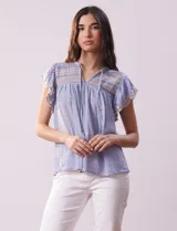 Blusa celeste de algodón con cuello a la base y escote en V con lazo de ajuste. Tiene mangas cortas amplias y bordados en la delantera, mangas y espalda.