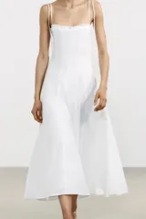 Vestido midi blanco de popelín con escote corazón y volantes. Tiene tirantes finos con detalle de lazo, forro interior combinado y cierre lateral con cremallera oculta.