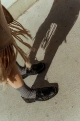 Mocasín de cuero color marrón con tachas metálicas plateadas en la puntera y laterales.