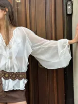 Blusa negra traslúcida con volados, mangas largas abullonadas y cierre frontal con botones.
