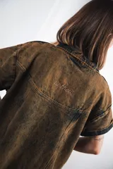 Vestido corto de denim celeste con cuello tipo camisa, cierre frontal metálico y bolsillos delanteros. Presenta bordados de soles y lunas en el canesú delantero y trasero.