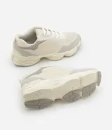 Championes dad sneaker grises con recortes en cuero sintético, cordones blancos y suela chunky de goma color crema.