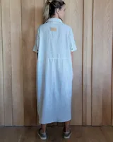 Vestido camisero de denim azul con cuello clásico, cierre frontal con botones y mangas cortas con dobladillo.