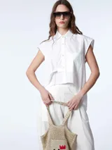 Camisa crop blanca con botones frontales y espalda de largo irregular, confeccionada en 100% algodón.