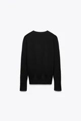 Sweater negro de punto liso con cuello redondo y mangas largas con botones dorados en los puños.