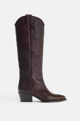 Bota alta de mujer color marrón oscuro, confeccionada en piel de efecto granulado. Presenta un diseño tipo cowboy con doble tirador en la caña para facilitar el calce (pull on) y un tacón medio de 5 cm. La punta es ligeramente afilada.