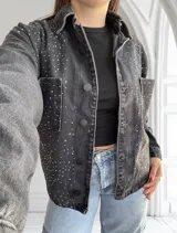 Campera de jean negra con tachas plateadas, corte recto, cuello camisero y cierre frontal con botones.