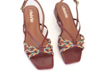 Sandalia de cuero color suela, con tiras finas y detalle frontal trenzado en colores celeste, naranja y amarillo. Pulsera ajustable con hebilla metálica y base plana con taco bajo geométrico.