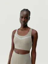 Top deportivo color beige con tirantes regulables cruzados en la espalda y cierre ajustable. Presenta una banda reflectante en el frente y copas extraíbles.