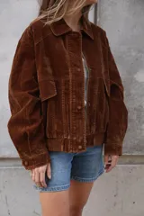 Campera estilo bomber o trucker de color mostaza/naranja quemado con efecto acid wash o desgastado. Presenta cuello camisero, cierre frontal y puños y cintura ajustados con elástico. Posee bolsillos frontales con solapa y botón.