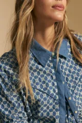 Camisa de manga larga, color azul, con cuello camisero y estampado geométrico en blanco. Presenta un diseño de doble capa: una camisa exterior abierta con botones y un top anudado debajo.