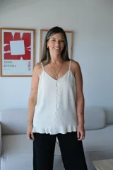 Musculosa color beige claro, con escote en V y tirantes finos ajustables. Presenta una hilera de botones blancos en el centro frontal y un ruedo con volado.