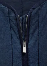 Chaqueta azul de estilo tejano vaquero con diseño acolchado y relleno. Tiene cuello redondo, cierre de cremallera frontal, dos bolsillos de ribete delanteros y mangas largas.