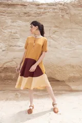 Vestido corto color mostaza con corte evasé y mangas cortas. Presenta un bloque de color marrón en la falda y otro bloque color beige en el ruedo.