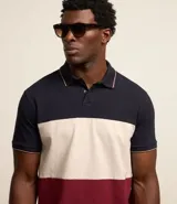 Polo de hombre de corte regular, confeccionada en algodón, con cuello clásico, mangas cortas y diseño de bloques de color: azul marino en la parte superior, blanco en el centro y rojo borgoña en la parte inferior.
