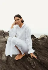 Camisa blanca de lino, de corte recto y cuello clásico. Tiene mangas largas abullonadas con frunces y puños elásticos.