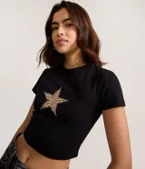 Remera negra de algodón con cuello redondo, manga corta y corte cropped ajustado al cuerpo. Presenta un aplique de estrella con estampado de leopardo en el pecho.