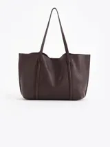 Cartera shopper negra de cuero vacuno flor, con grabados de cerezas distribuidos en la superficie. Tiene acceso mediante imán, manijas de cuero y un tag con mini aplique de cereza. Incluye un bolsillo desmontable con cierre metálico en su interior.