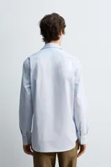 Camisa celeste de algodón con estructura twill, corte regular, cuello solapa, manga larga con puños abotonados y cierre frontal con botones.