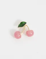 Broche con forma de cerezas rosadas con glitter, hoja verde y detalles dorados.