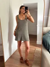 Vestido corto de tejido de punto color beige/dorado, con escote redondo y tirantes anchos. Presenta un tejido acanalado verticalmente con hilos de lurex que le dan brillo.